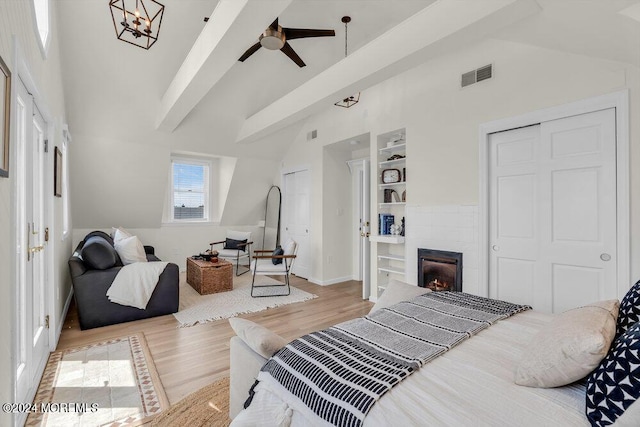 bedroom with high vaulted ceiling, a closet, beam ceiling, a tiled fireplace, and light hardwood / wood-style floors