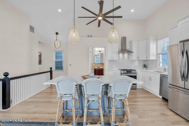 kitchen with stainless steel appliances, wall chimney range hood, and white cabinets