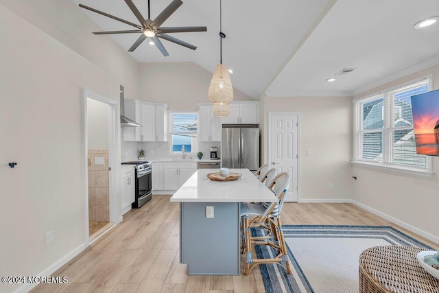 kitchen with white cabinets, appliances with stainless steel finishes, a kitchen island, and wall chimney range hood