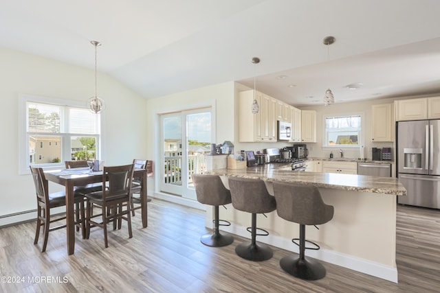 kitchen with a kitchen breakfast bar, vaulted ceiling, appliances with stainless steel finishes, light stone counters, and kitchen peninsula