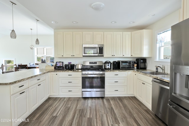 kitchen featuring pendant lighting, sink, dark hardwood / wood-style floors, kitchen peninsula, and stainless steel appliances