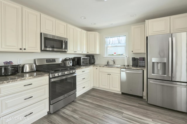 kitchen with appliances with stainless steel finishes, dark hardwood / wood-style flooring, dark stone counters, and sink