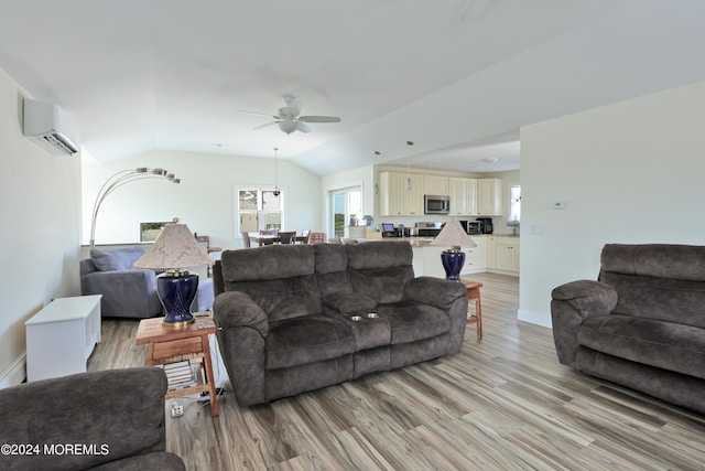 living room featuring vaulted ceiling, light hardwood / wood-style flooring, an AC wall unit, and ceiling fan