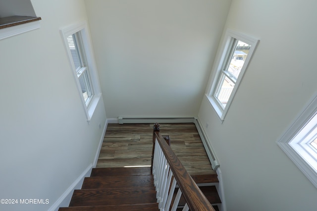 staircase with plenty of natural light, a baseboard radiator, and wood-type flooring