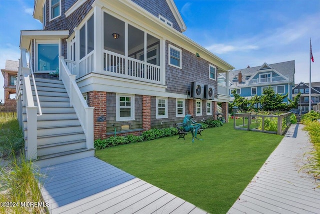 rear view of house with a sunroom, a wooden deck, and a lawn