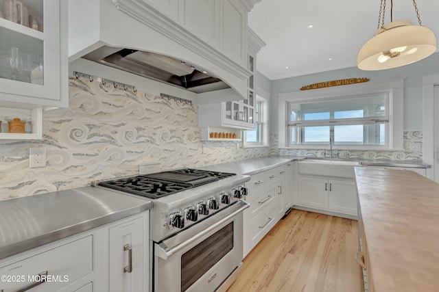 kitchen featuring decorative backsplash, custom exhaust hood, pendant lighting, white cabinets, and stainless steel stove