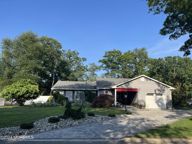 ranch-style house with an attached garage, fence, a front lawn, and decorative driveway