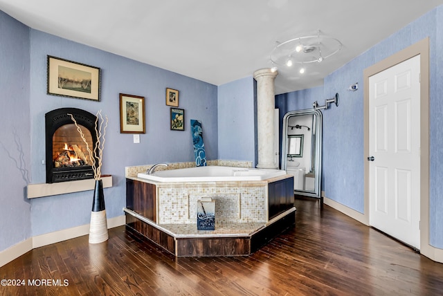 bathroom with a fireplace, a bath, decorative columns, and hardwood / wood-style floors