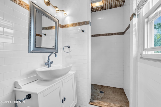 bathroom with vanity, tiled shower, and tile walls