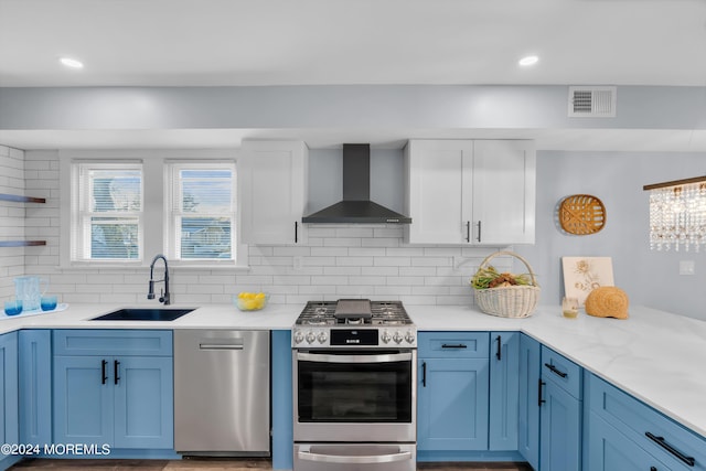 kitchen with backsplash, sink, wall chimney exhaust hood, blue cabinetry, and stainless steel appliances