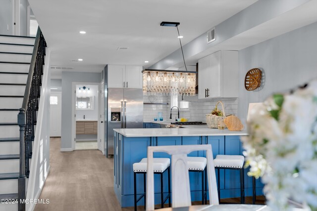 kitchen featuring hanging light fixtures, stainless steel fridge, tasteful backsplash, a notable chandelier, and white cabinetry