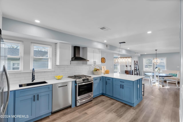 kitchen featuring kitchen peninsula, stainless steel appliances, sink, wall chimney range hood, and hanging light fixtures