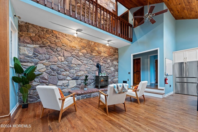 living room with ceiling fan, light hardwood / wood-style flooring, high vaulted ceiling, wooden ceiling, and a wood stove