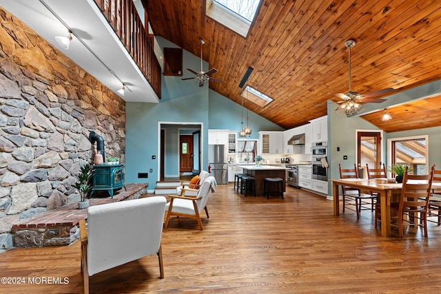 living room featuring a skylight, wood ceiling, light hardwood / wood-style flooring, high vaulted ceiling, and a wood stove