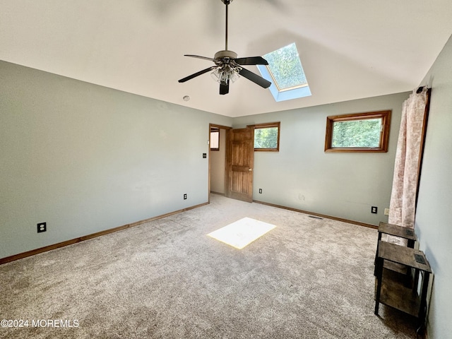 unfurnished bedroom with ceiling fan, lofted ceiling with skylight, and light carpet