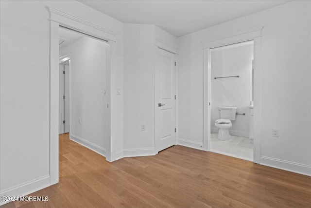 unfurnished bedroom featuring light wood-style floors, ensuite bath, and baseboards