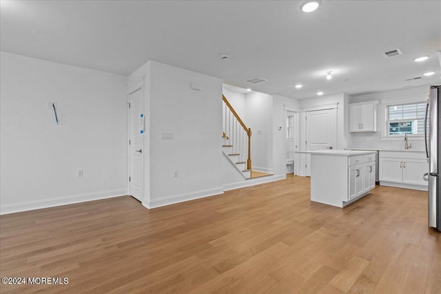 kitchen with sink, stainless steel fridge, white cabinets, a center island, and light wood-type flooring