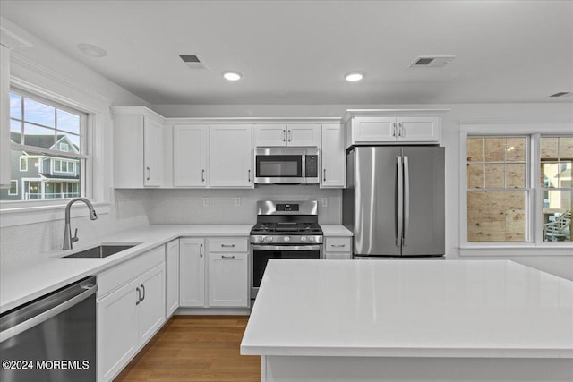 kitchen featuring appliances with stainless steel finishes, tasteful backsplash, sink, white cabinets, and light wood-type flooring