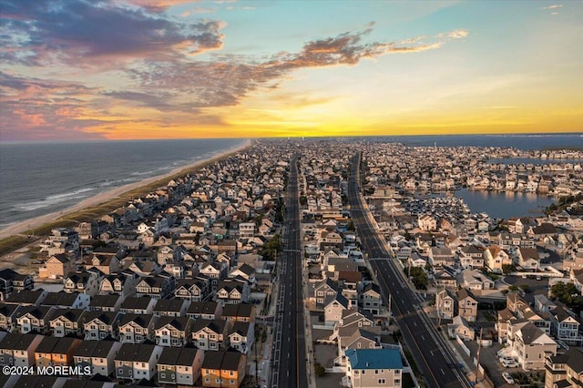 aerial view at dusk featuring a water view and a beach view