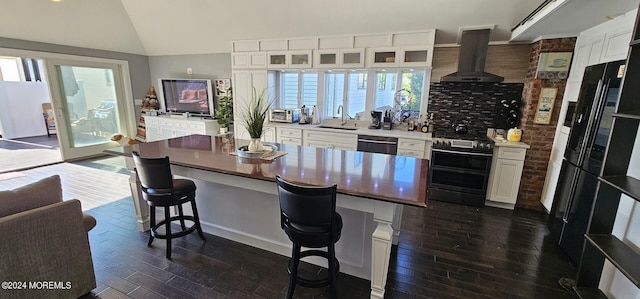 kitchen with white cabinets, a kitchen breakfast bar, wall chimney range hood, and appliances with stainless steel finishes