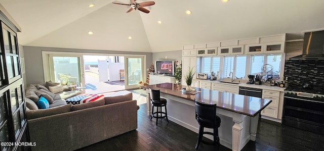 kitchen featuring a breakfast bar, a center island, wall chimney range hood, sink, and white cabinetry