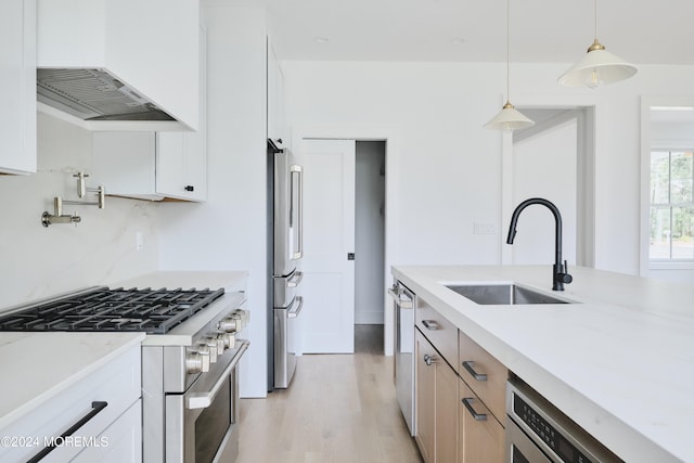 kitchen featuring light stone countertops, premium appliances, white cabinetry, sink, and hanging light fixtures