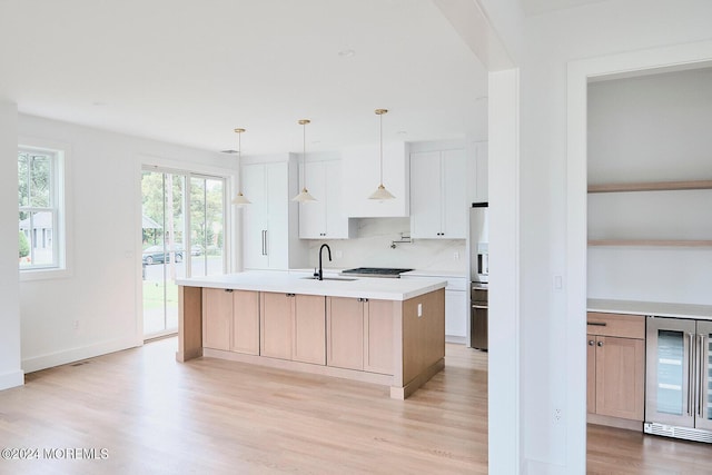 kitchen featuring appliances with stainless steel finishes, a kitchen island with sink, wine cooler, white cabinets, and sink