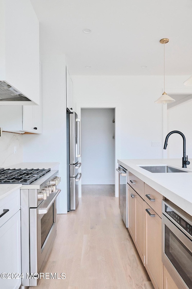 kitchen with light hardwood / wood-style floors, pendant lighting, sink, white cabinetry, and high quality appliances