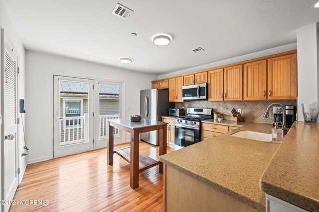 kitchen with sink, stainless steel appliances, light hardwood / wood-style floors, decorative backsplash, and kitchen peninsula