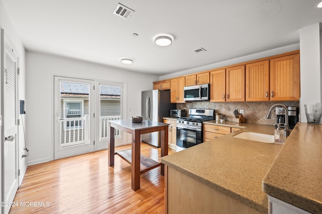 kitchen featuring visible vents, light wood finished floors, a sink, stainless steel appliances, and backsplash