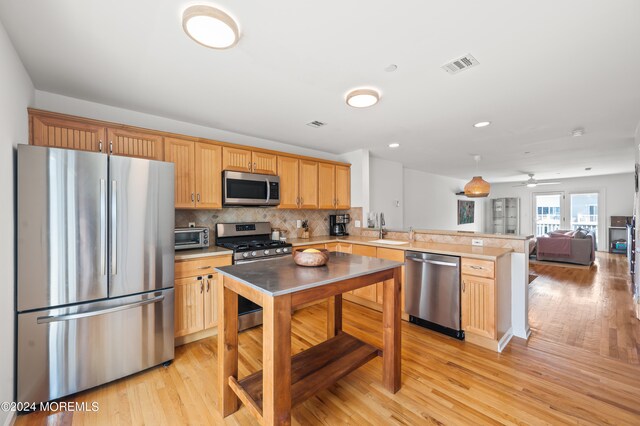 kitchen with sink, tasteful backsplash, light hardwood / wood-style flooring, appliances with stainless steel finishes, and kitchen peninsula