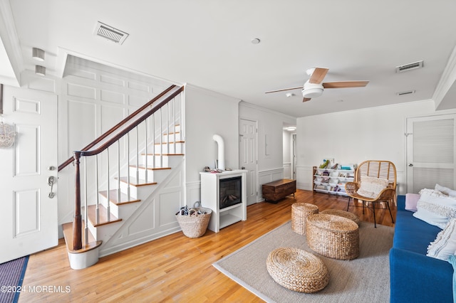 living room with crown molding, light wood-style flooring, a decorative wall, and visible vents