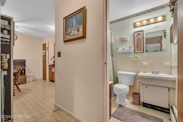 bathroom featuring tile walls, tile patterned flooring, toilet, vanity, and a baseboard heating unit