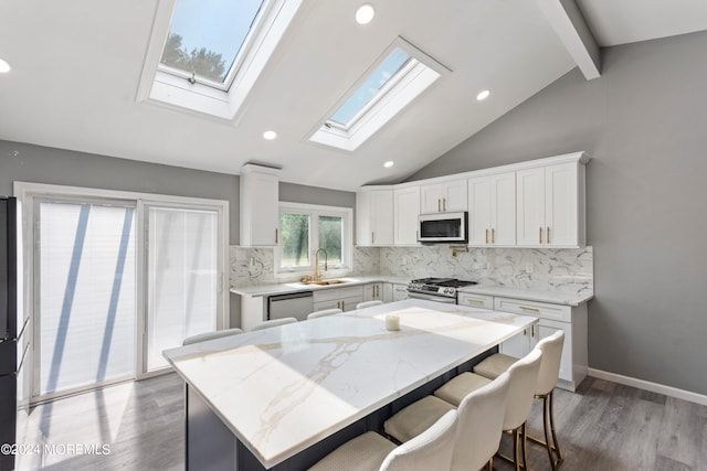 kitchen featuring a skylight, white cabinets, appliances with stainless steel finishes, wood-type flooring, and sink