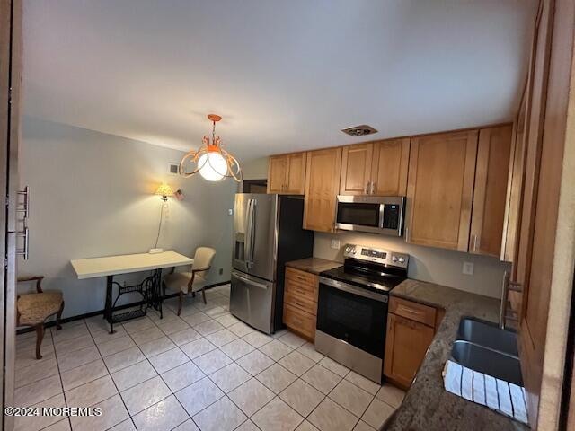 kitchen with light tile patterned floors, sink, stainless steel appliances, and hanging light fixtures