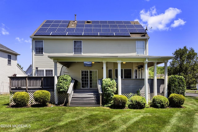 back of property with a wooden deck, a lawn, and solar panels