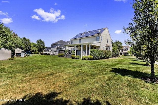 rear view of house featuring a yard, solar panels, and a playground