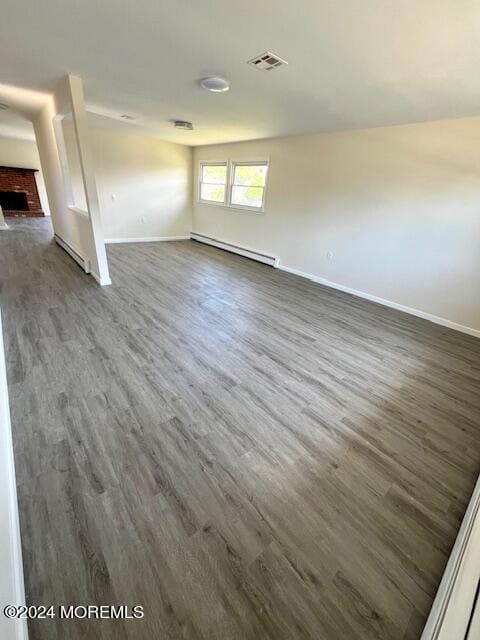 unfurnished room with baseboard heating, dark wood-type flooring, and a brick fireplace