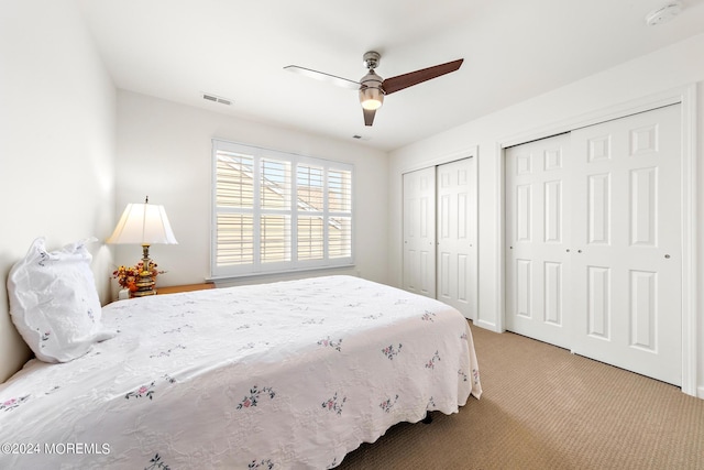 bedroom with ceiling fan, light colored carpet, and multiple closets