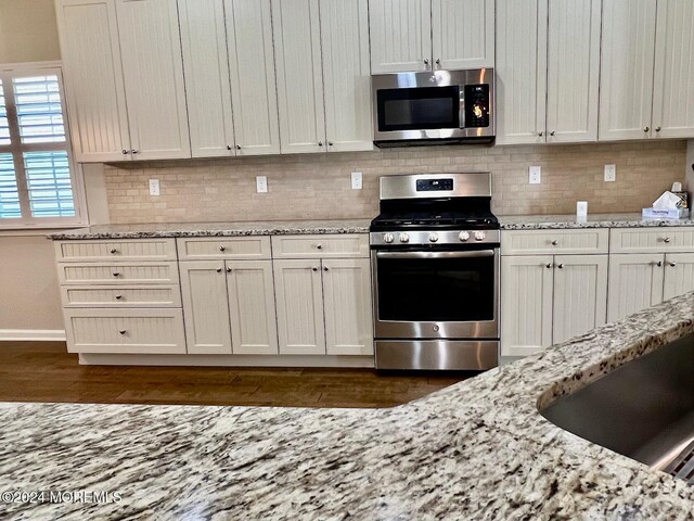 kitchen with light stone countertops, white cabinetry, appliances with stainless steel finishes, and dark hardwood / wood-style flooring