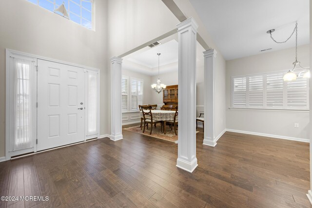 entryway featuring a notable chandelier, a raised ceiling, ornate columns, and dark wood-type flooring