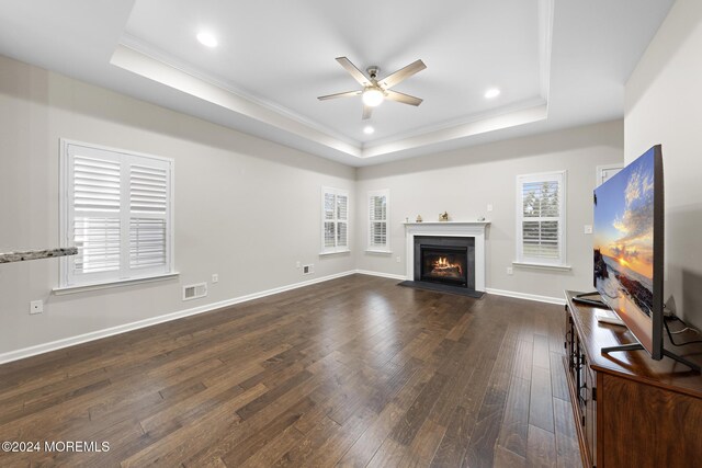 living room with ceiling fan, a tray ceiling, dark hardwood / wood-style floors, and ornamental molding