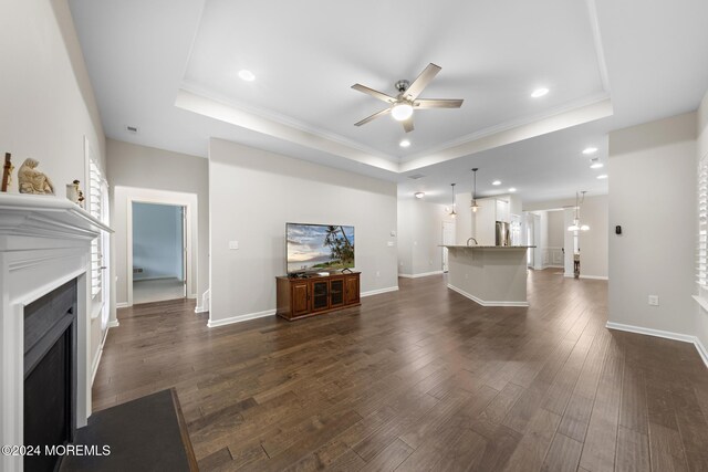 unfurnished living room featuring ceiling fan with notable chandelier, a tray ceiling, dark hardwood / wood-style flooring, and crown molding