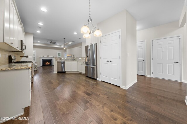 kitchen with appliances with stainless steel finishes, white cabinetry, pendant lighting, ceiling fan, and light stone counters