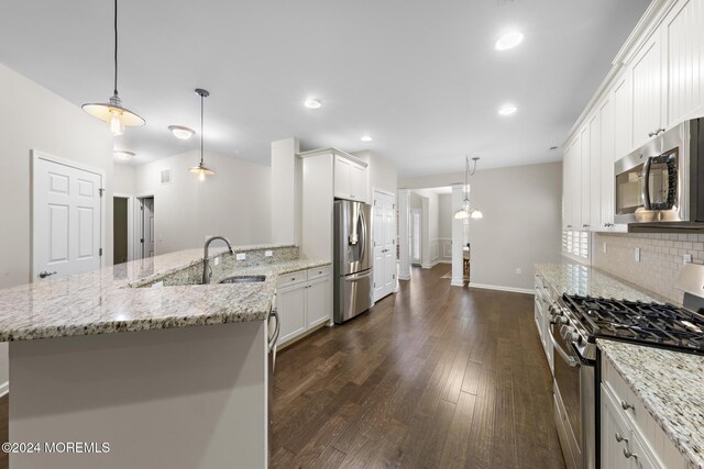 kitchen with hanging light fixtures, appliances with stainless steel finishes, sink, white cabinetry, and a center island with sink