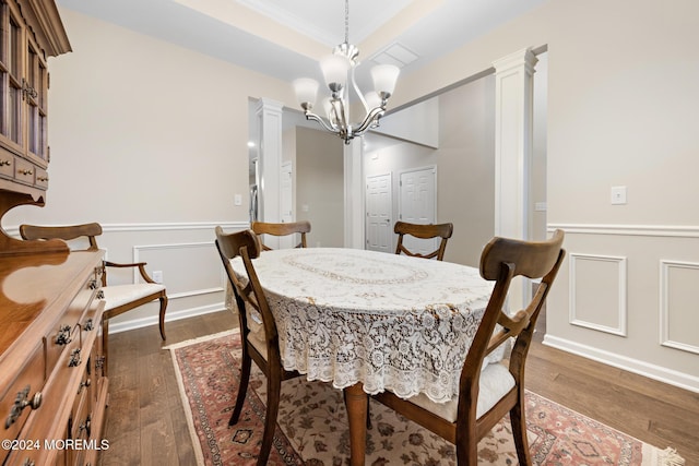 dining room featuring decorative columns, dark wood-type flooring, ornamental molding, and an inviting chandelier