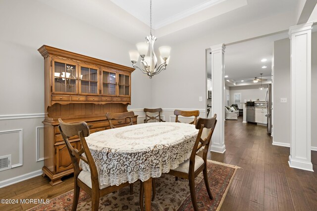 dining room featuring ceiling fan with notable chandelier, a tray ceiling, dark hardwood / wood-style flooring, and ornate columns