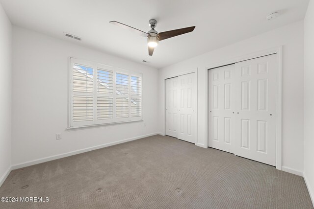 unfurnished bedroom with ceiling fan, light colored carpet, and two closets