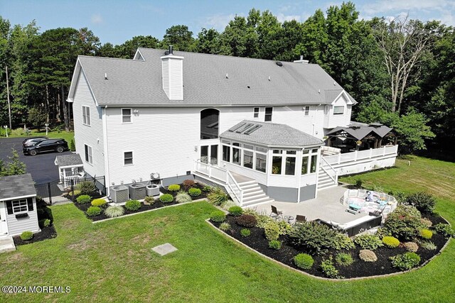 rear view of house with a lawn, a deck, central AC unit, a sunroom, and a patio