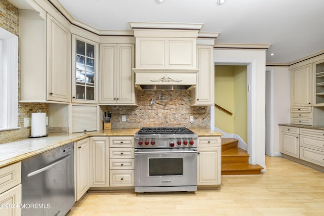 kitchen featuring cream cabinets, stainless steel appliances, light stone countertops, light hardwood / wood-style floors, and backsplash